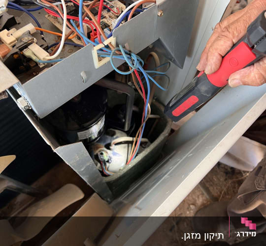 אדם מתקן מזגן עם כלי עבודה וחוטי חשמל